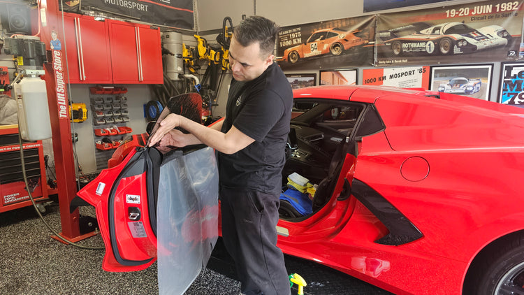 Professional installing window tinting on a red Corvette.