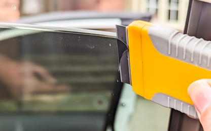 Professional using a scraper to carefully remove window tinting, demonstrating the process of window tint removal. The image visually guides on how to remove window tint effectively.